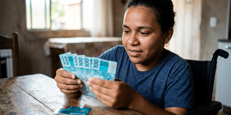 Mulher cadeirante conta notas de R$ 100 em ambiente doméstico.