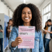 Estudante sorridente exibe caderno do ENEM 2020 em corredor escolar.