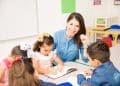 Professora sorridente acompanha crianças em atividade escolar.