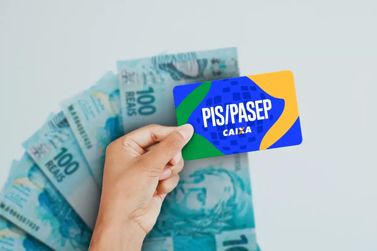 Mão segurando cartão azul PIS/Pasep da Caixa com fundo de notas de R$ 100 reais espalhadas, simbolizando o pagamento do Abono Salarial PIS/Pasep 2026.