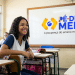 Estudante sorrindo em sala de aula com logo do programa Pé-de-Meia.