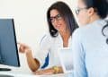 Duas mulheres em escritório, uma de blusa branca aponta para monitor enquanto outra de camisa azul observa atentamente, simbolizando a diferença entre RH e Departamento pessoal.