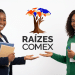 Duas jovens negras sorrindo e apontando para logo do Raízes Comex, uma com blazer e livros, outra com blusa verde e caderno.
