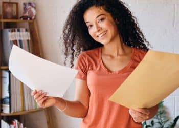 Jovem sorridente segura carta e envelope em casa.
