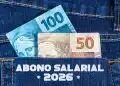 Abono salarial 2026: cédulas de cem e cinquenta reais saindo do bolso traseiro de uma calça jeans com a inscrição abono salarial 2026 estampada no tecido