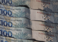 Cédulas de 100 reais empilhadas mostrando detalhes do Banco Central do Brasil e elementos de segurança, simbolizando o pagamento de até R$ 4.521.