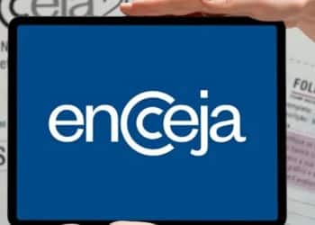Mão segurando celular exibindo logotipo do Encceja com cartão de prova ao fundo