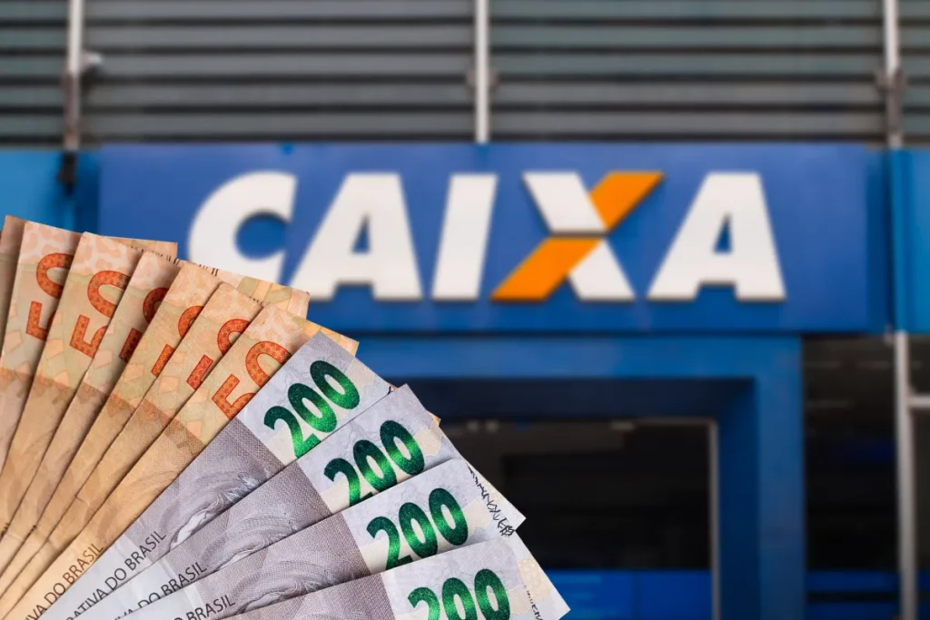Notas de real em frente a uma agência da Caixa, ilustrando o pagamento do Saque Calamidade do FGTS de até R$ 6.220.