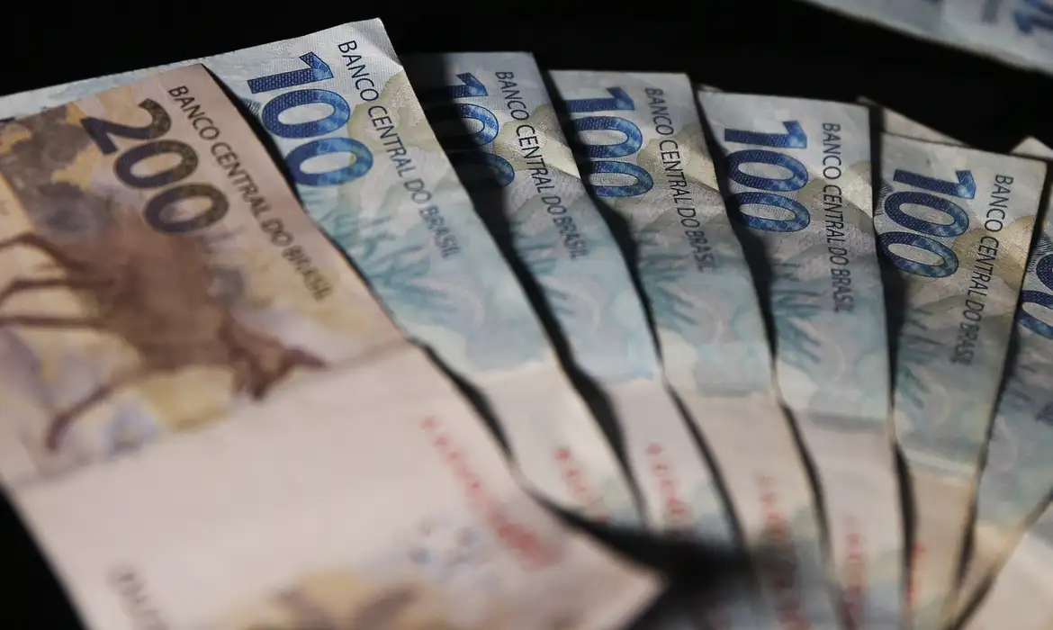 Cédulas de duzentos e cem reais dispostas em formato de leque sobre fundo escuro