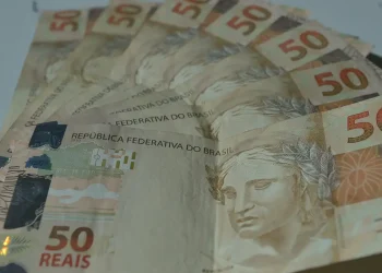 Leque de cédulas de cinquenta reais espalhadas sobre superfície clara em close que destaca o dinheiro em espécie