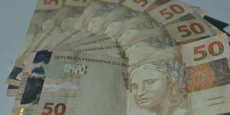 Leque de cédulas de cinquenta reais espalhadas sobre superfície clara em close que destaca o dinheiro em espécie