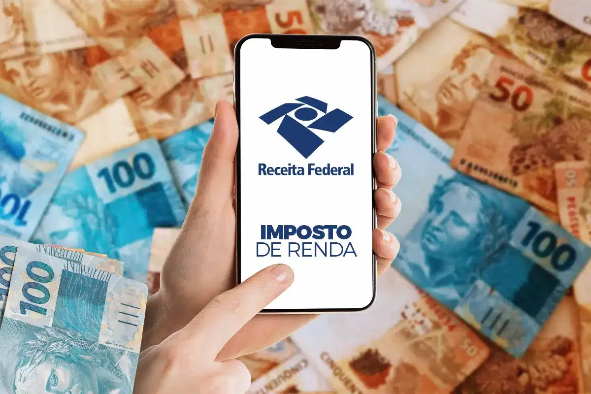 Mão segura smartphone com logo da Receita Federal e texto "Imposto de Renda" sobre notas de real