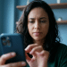Mulher observa a tela do celular com expressão concentrada, sentada em ambiente interno