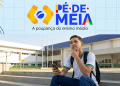 Estudante do ensino médio consulta o celular em frente a uma escola pública, com a logomarca do Pé-de-Meia