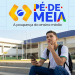 Estudante do ensino médio consulta o celular em frente a uma escola pública, com a logomarca do Pé-de-Meia