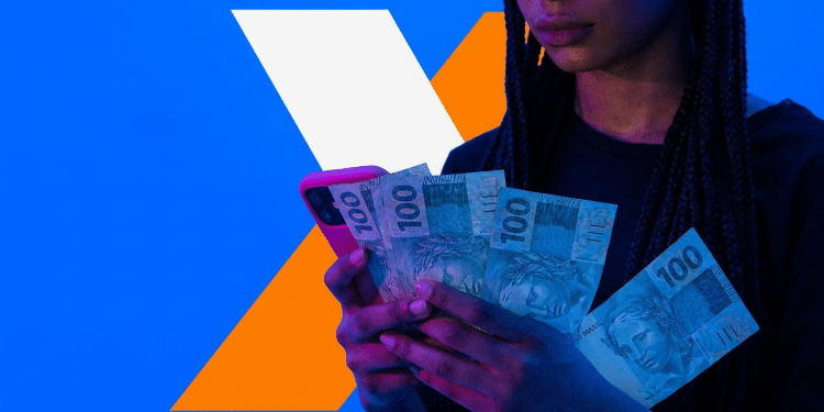 Mulher segura cédulas de R$ 100 e celular durante consulta ao aplicativo da Caixa