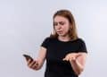 Mulher de camiseta preta com expressão de surpresa enquanto observa a tela do celular