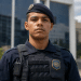 Agente da Guarda Municipal com uniforme azul-marinho, boina com brasão, colete tático e rádio comunicador.