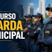 Guardas Municipais fardados de azul perfilados ao lado de viatura com o texto "Concurso Guarda Municipal"