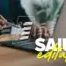 Mão segurando caneta stylus sobre laptop com ícones holográficos de checklist e texto "SAIU edital!" em destaque.