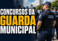Agentes da Guarda Municipal em formação, usando uniformes azuis com coletes táticos e quepes, em área urbana.