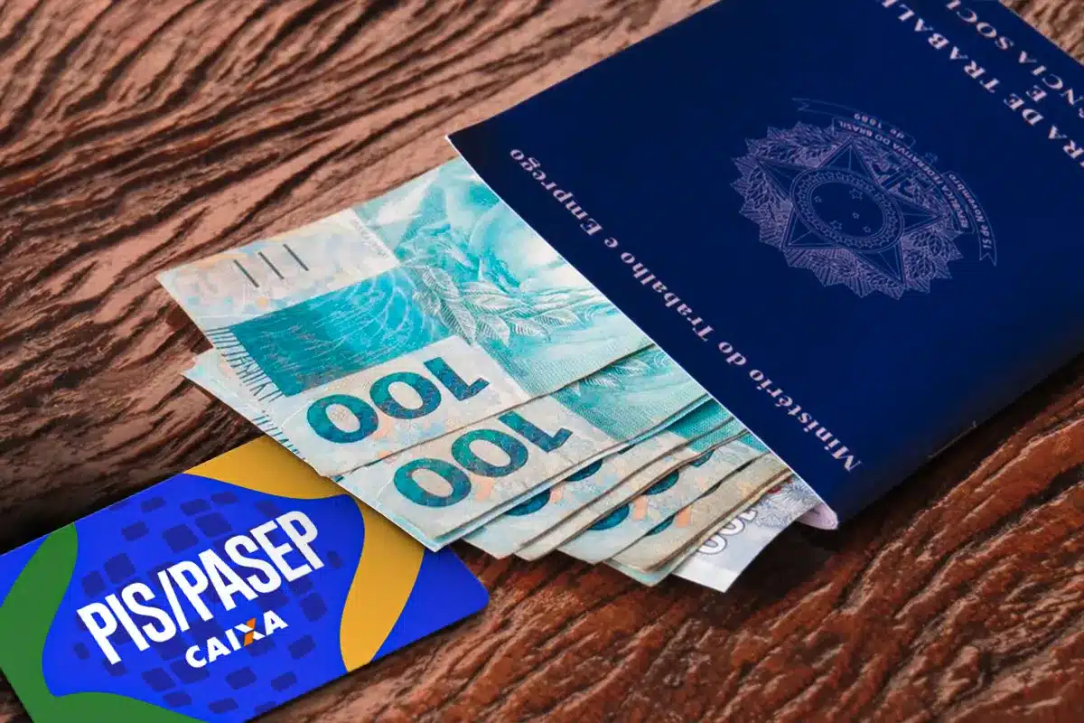 Carteira de Trabalho brasileira ao lado de leque de notas de cem reais com letreiro PIS Pasep em destaque