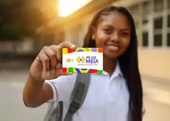 Estudante uniformizada segurando o cartão do programa Pé-de-Meia em frente à escola, representando os critérios para receber o benefício pago pelo governo federal.