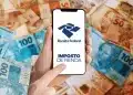 Mão segura celular com tela da Receita Federal e texto "Imposto de Renda" sobre notas de Real.