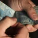 Mãos manuseando cédulas de cem reais brasileiros sobre fundo escuro em close-up
