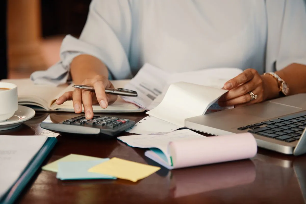 Pessoa usa calculadora e confere boletos sobre a mesa enquanto organiza as contas para renegociar dívidas pelo Novo Desenrola