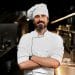 Chef de cozinha com uniforme branco e braços cruzados em cozinha