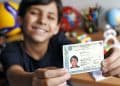 Adolescente sorri e mostra a Carteira de Identidade Nacional segurando o documento com as duas mãos.