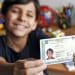 Adolescente sorri e mostra a Carteira de Identidade Nacional segurando o documento com as duas mãos.