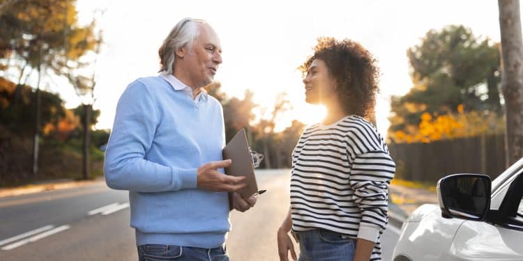 Homem mais velho e mulher jovem conversam de forma tranquila e sorridente ao lado de um carro, ilustrando os traços de personalidade de quem agradece no trânsito segundo especialistas
