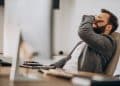 Homem de barba sentado em uma cadeira de escritório com a mão no rosto em expressão de bloqueio mental, representando o esquecimento momentâneo de palavras