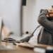 Homem de barba sentado em uma cadeira de escritório com a mão no rosto em expressão de bloqueio mental, representando o esquecimento momentâneo de palavras