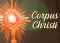 Ostensório dourado com raios solares exibindo hóstia consagrada e texto "Corpus Christi" em fundo marrom