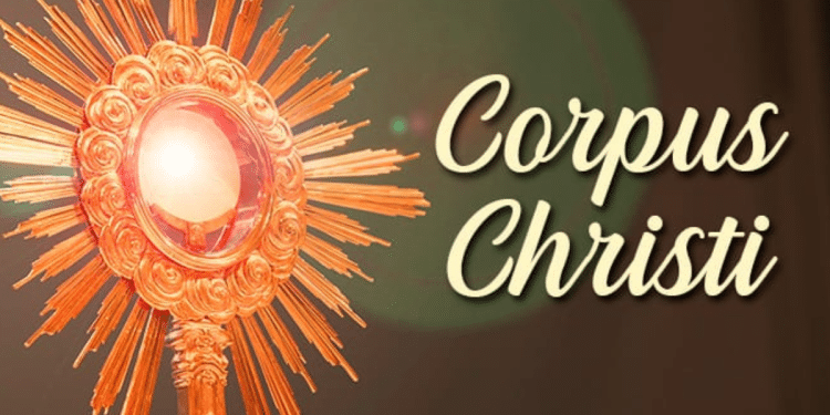 Ostensório dourado com raios solares exibindo hóstia consagrada e texto "Corpus Christi" em fundo marrom