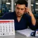Trabalhador analisa calendário de maio de 2026 em ambiente industrial ao lado de documentos e cartão de ponto sobre direitos no feriado de 23 de maio.