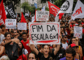 Manifestantes erguem cartazes pedindo fim da escala 6x1 na Avenida Paulista, com bandeiras vermelhas e brancas ao fundo.