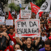 Manifestantes erguem cartazes pedindo fim da escala 6x1 na Avenida Paulista, com bandeiras vermelhas e brancas ao fundo.