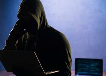 Pessoa encapuzada usando notebook em ambiente escuro