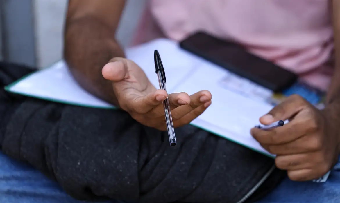 Estudante segura caneta sobre o caderno enquanto se prepara para o Exame Nacional do Ensino Médio