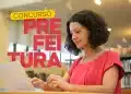 Mulher de blusa rosa digitando em notebook em ambiente de biblioteca com prateleiras de livros ao fundo