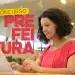 Mulher de blusa rosa digitando em notebook em ambiente de biblioteca com prateleiras de livros ao fundo