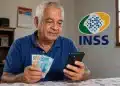 Aposentado brasileiro mexendo no celular e segurando notas de real, representando a consulta do 13º salário antecipado do INSS.