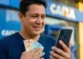 Homem consulta o celular em frente à agência da CAIXA enquanto segura notas de real, representando a liberação antecipada do Saque-Aniversário.