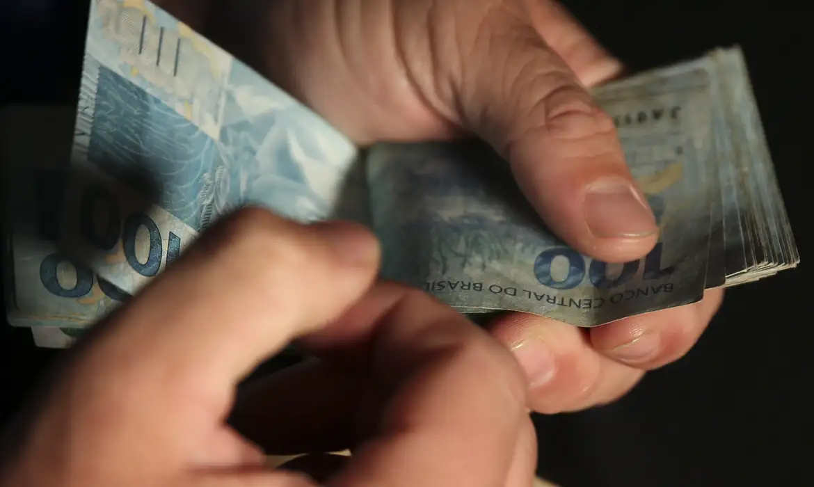 Mãos contando notas de cem reais durante o pagamento da primeira parcela do 13º salário do INSS
