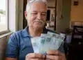 Aposentado brasileiro segura notas de R$ 100 em casa, representando o pagamento para quem recebe acima do salário mínimo a partir de 1º de junho.