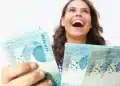 Mulher sorrindo segura notas de R$ 100 ao representar pagamento de R$ 1.486 ou mais para brasileiros com CPF de finais de 0 a 9.